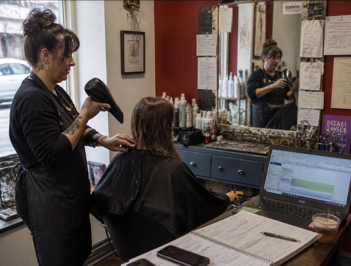A stylist working on a client in a small independent salon, appointment book and laptop on the counter